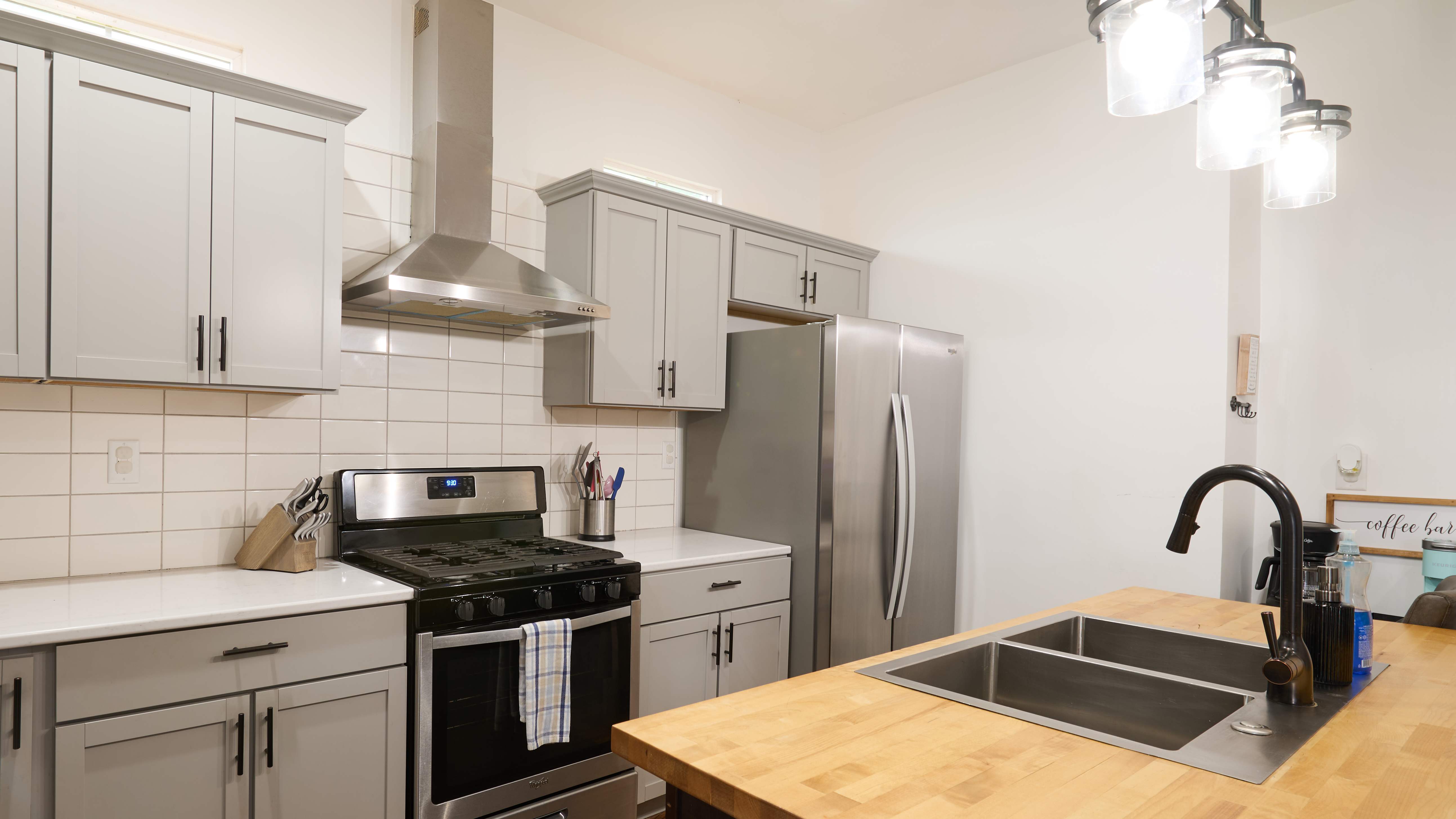 Modern kitchen with gray cabinets, a stainless steel oven and refrigerator, tile backsplash, and a wood island countertop.