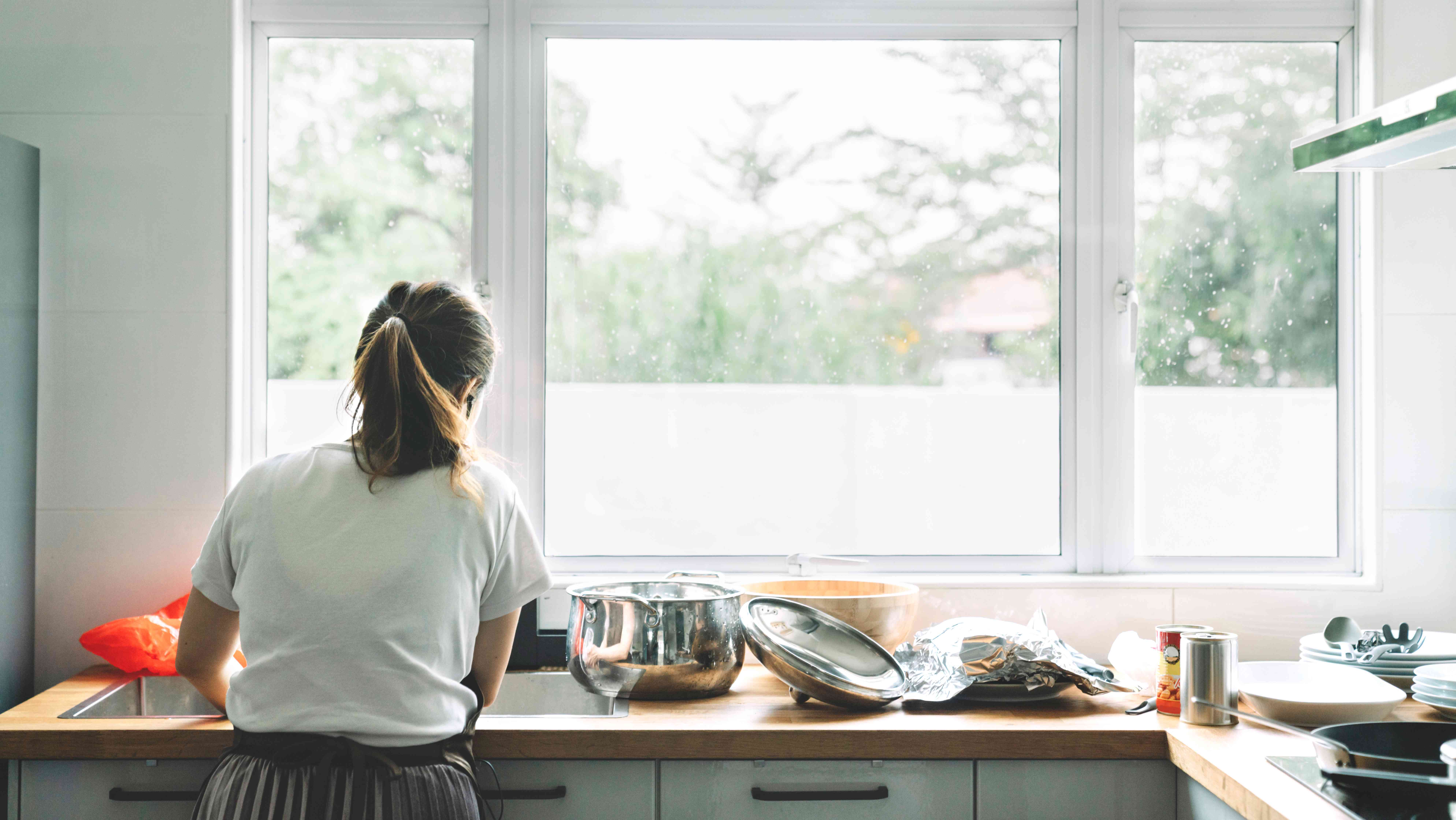 Woman standing in front of a large casement window is washing dishes