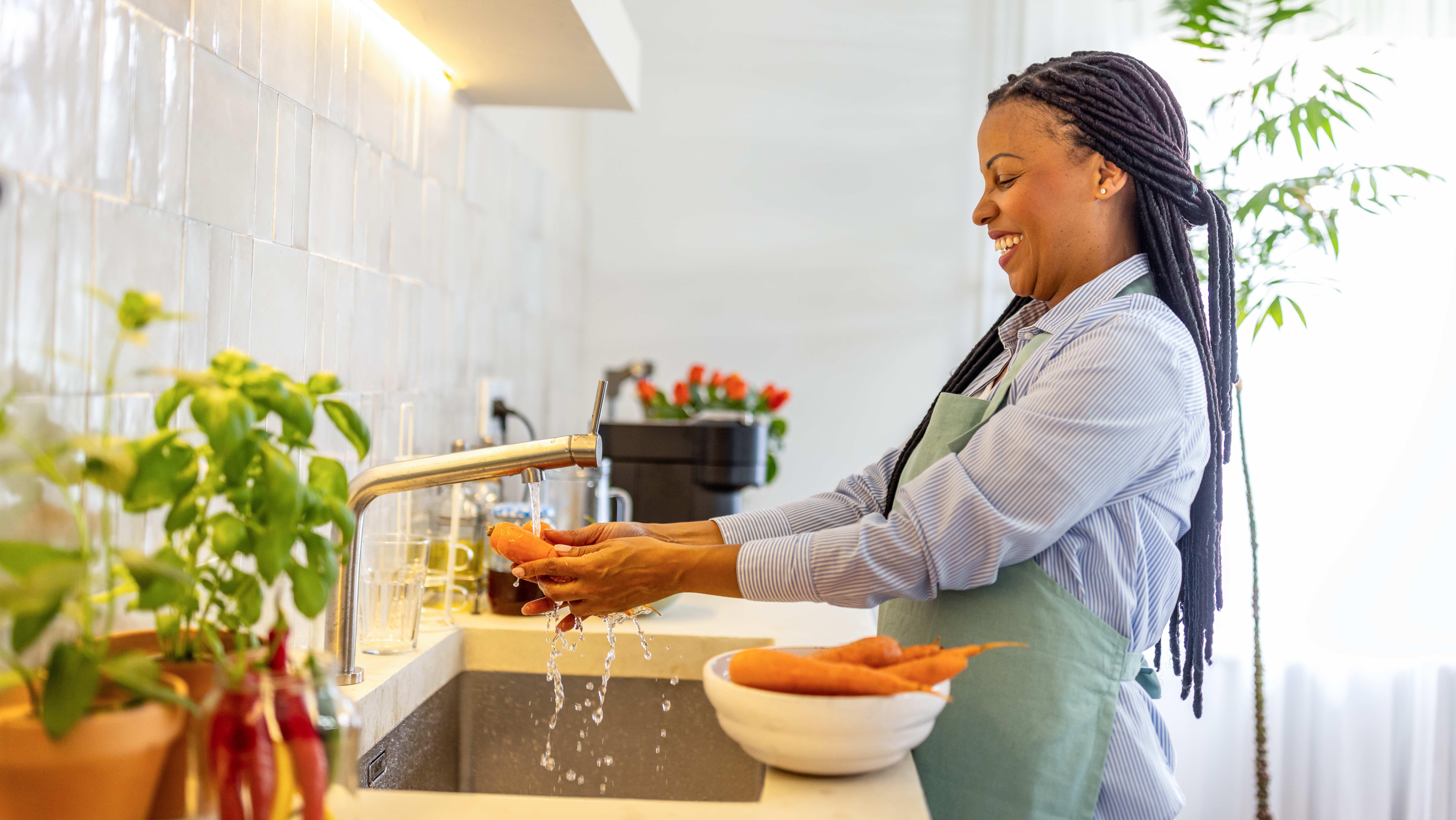 Smiling woman washing carrots in the kitchen sink
