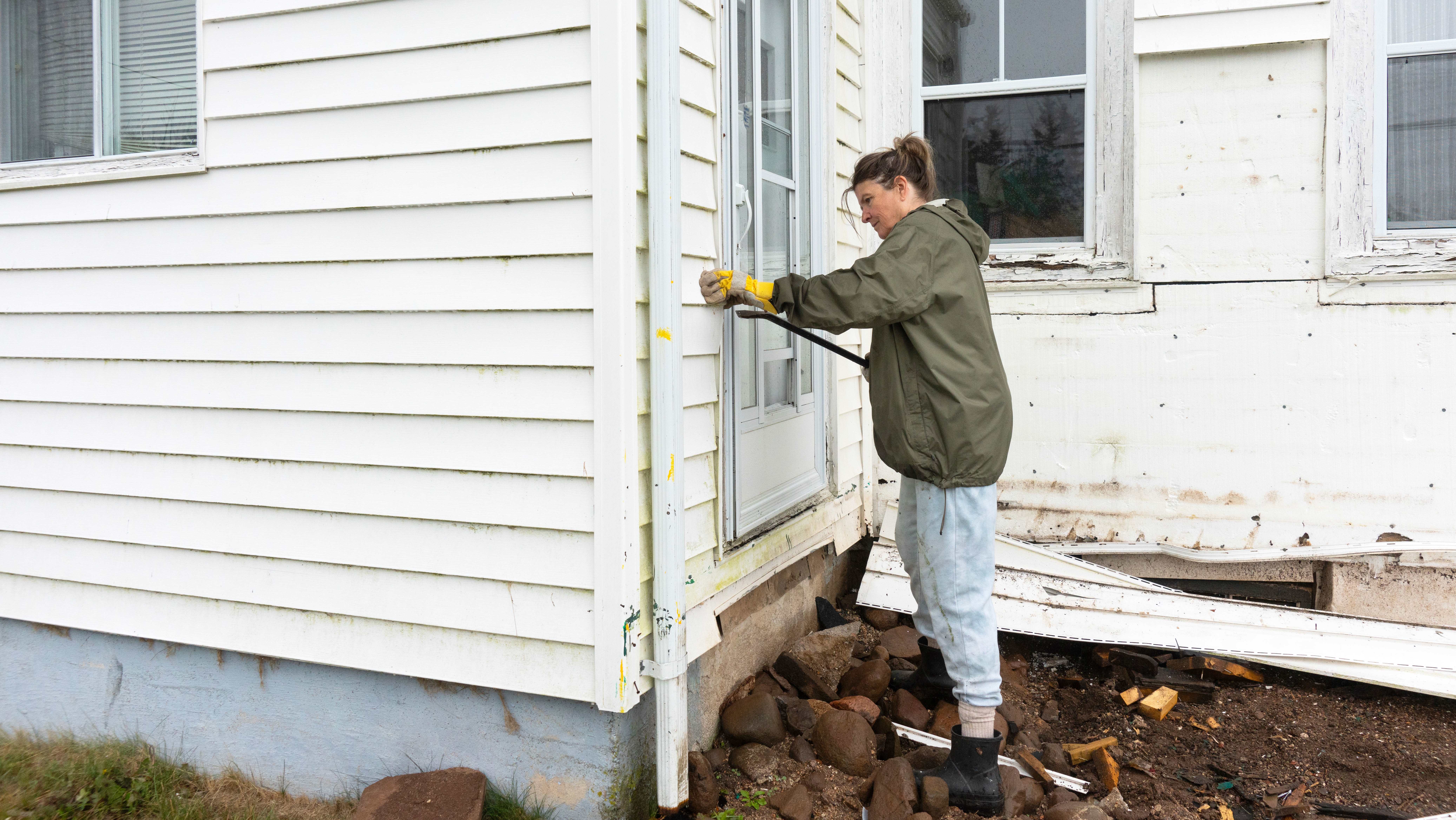 Woman removing old vinyl siding from a house