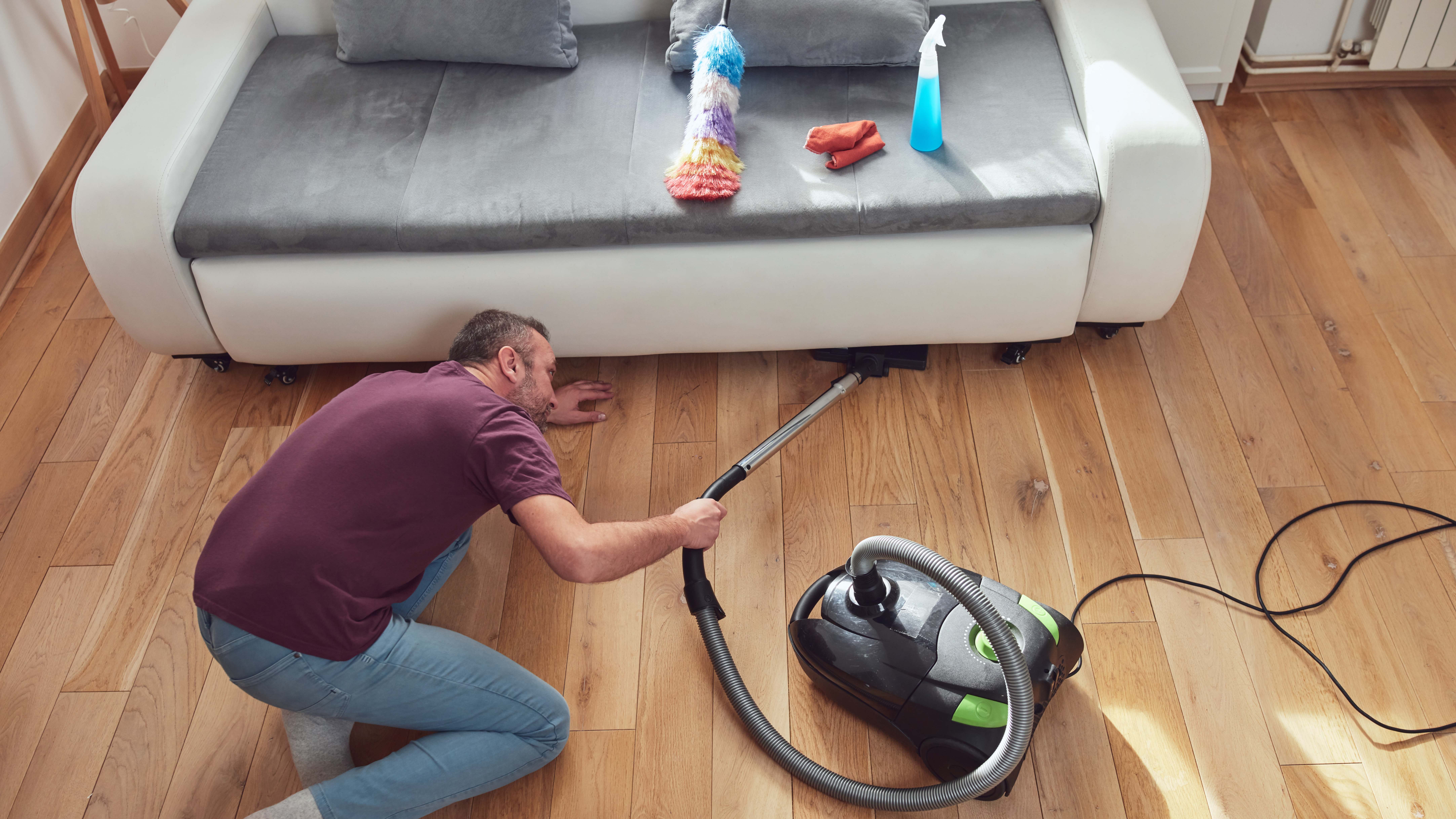 Man using a vacuum cleaner to clean under the sofa 