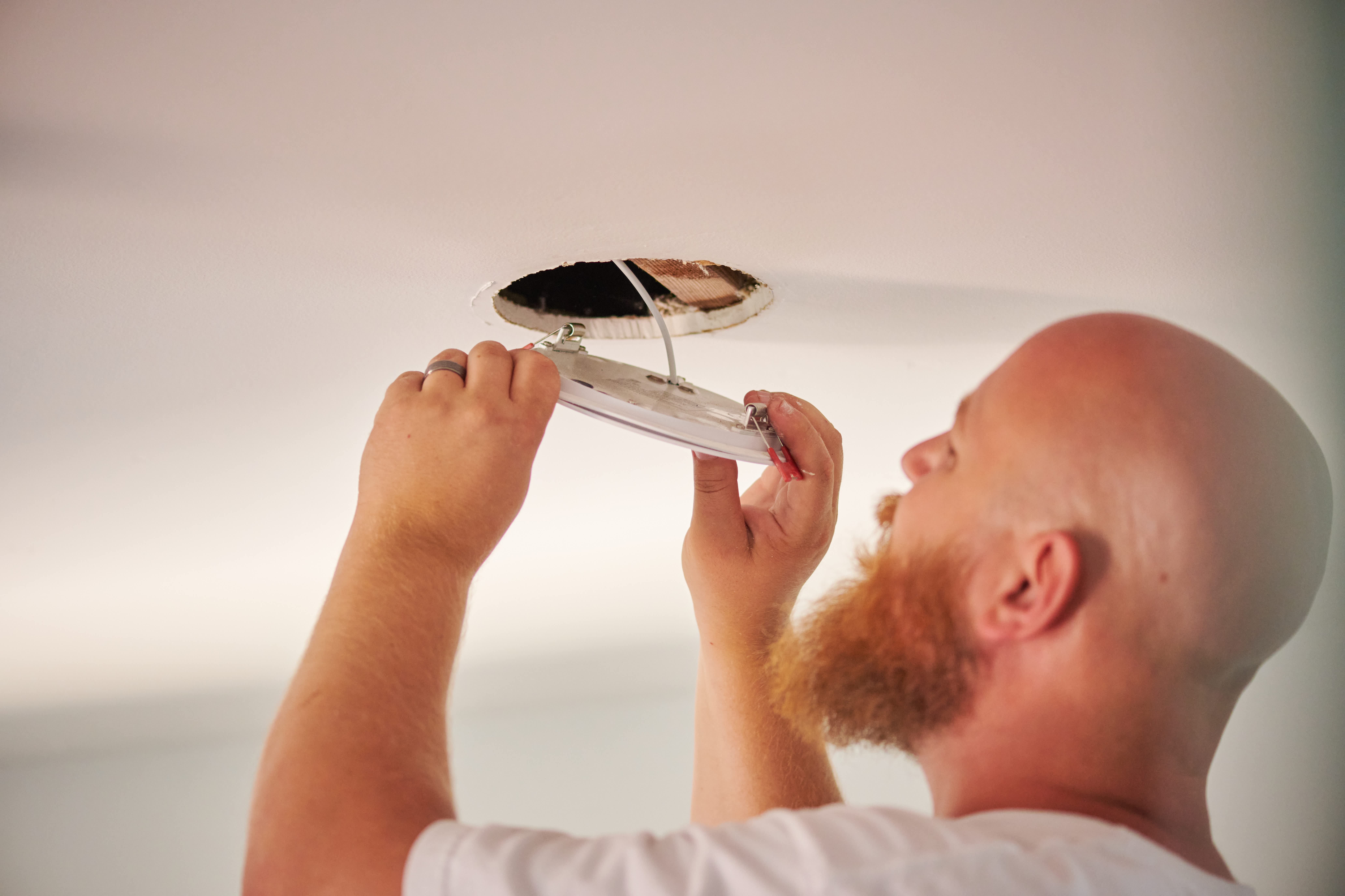 Handyman Chris McNeill from C.A. Shamrock LLC carefully installs a ceiling light fixture, aligning the wiring to ensure a secure fit in the ceiling.