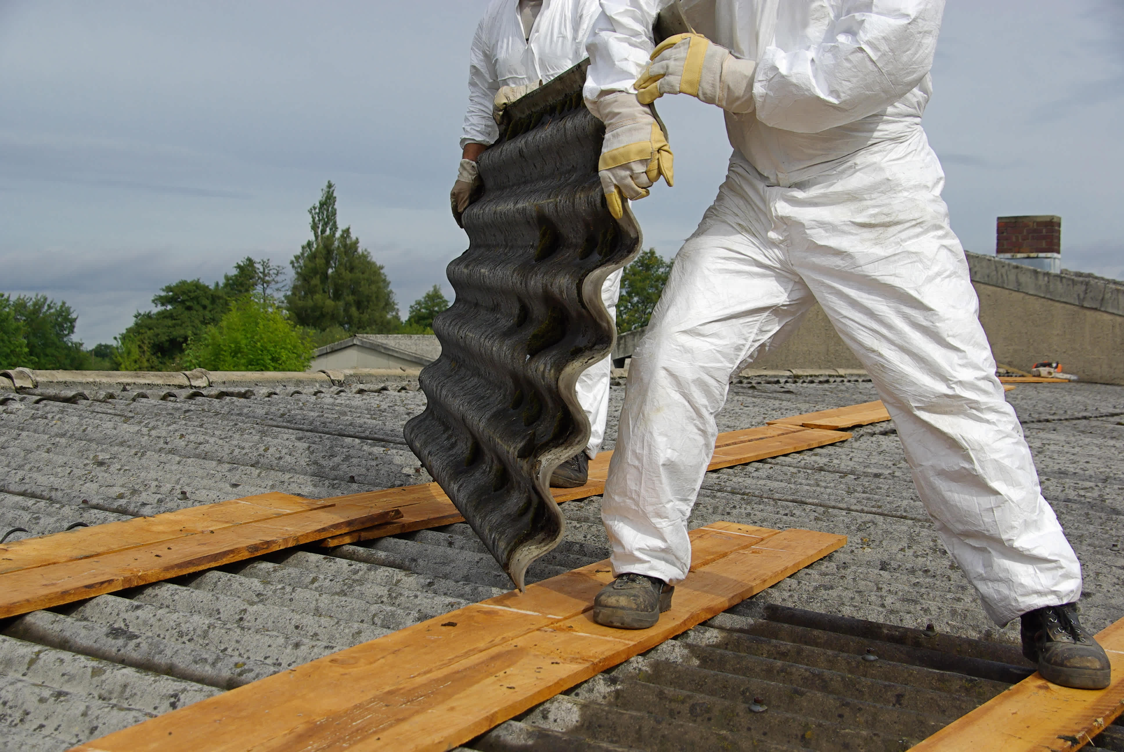 A worker in protective gear removes asbestos from an old building, emphasizing the importance of safe asbestos removal procedures.