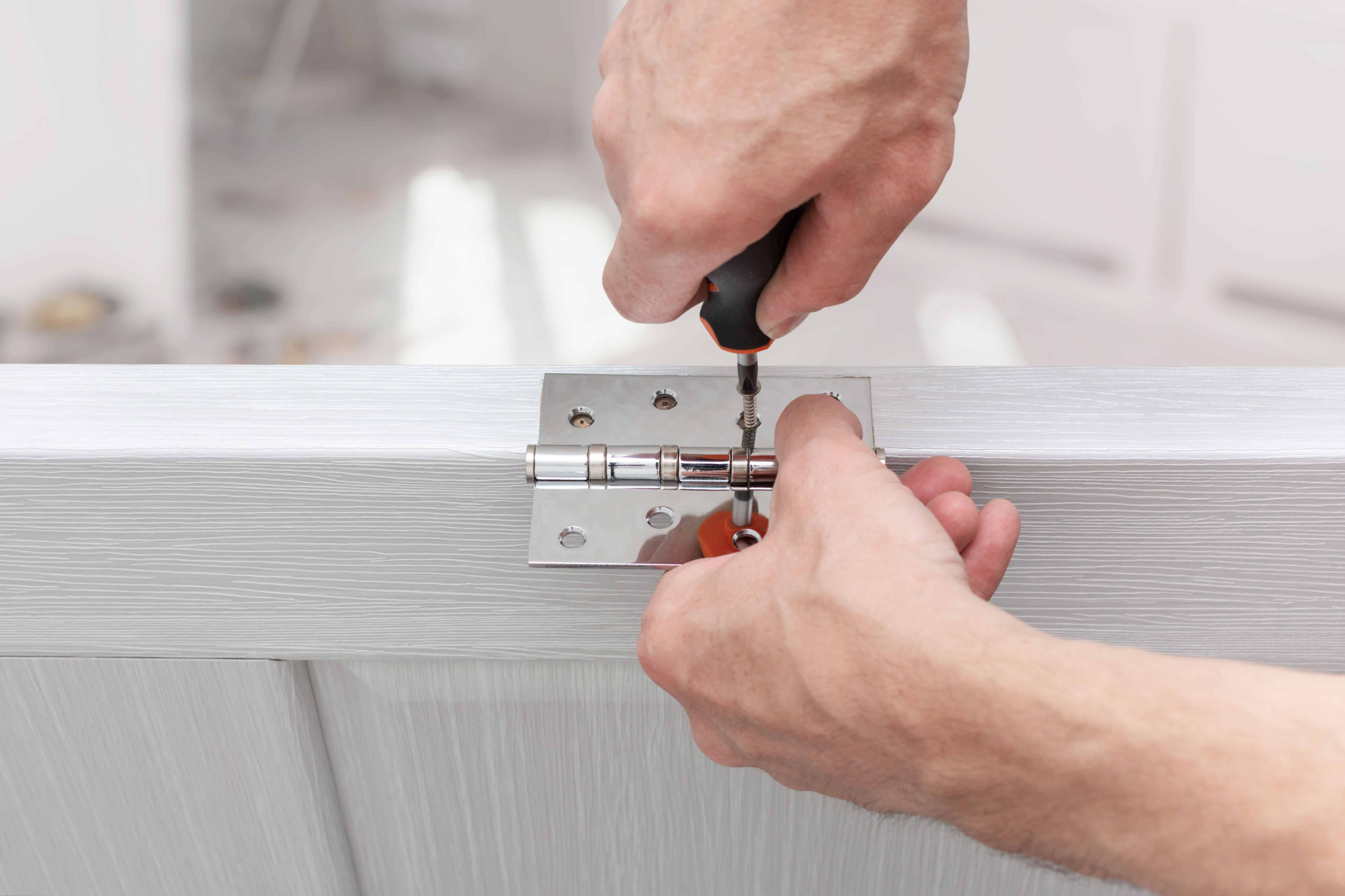 Worker installing a door hinge with a screwdriver, focusing on precision and alignment during a door repair task