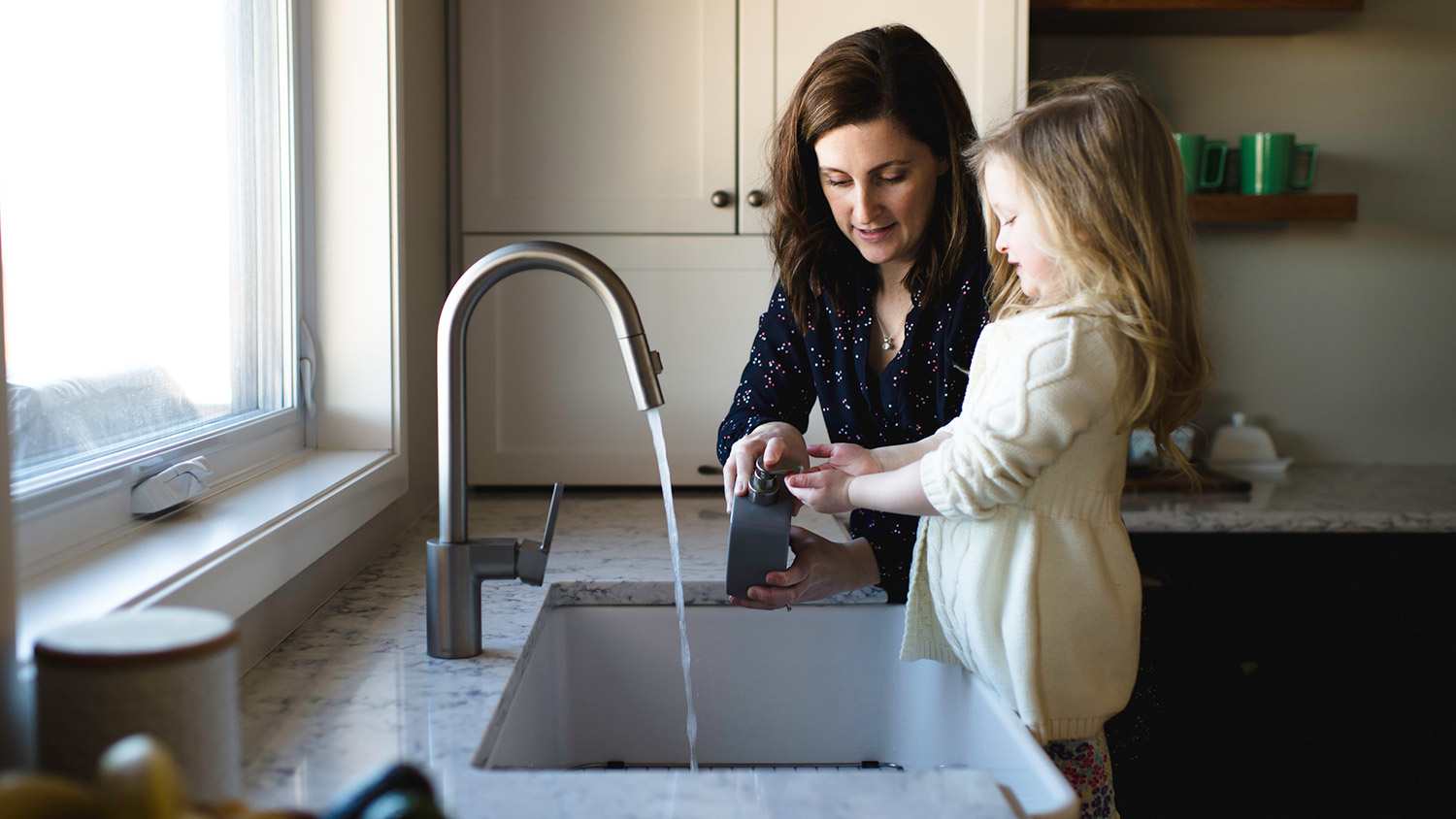 Mom and daughter wash hands at kitchen sink