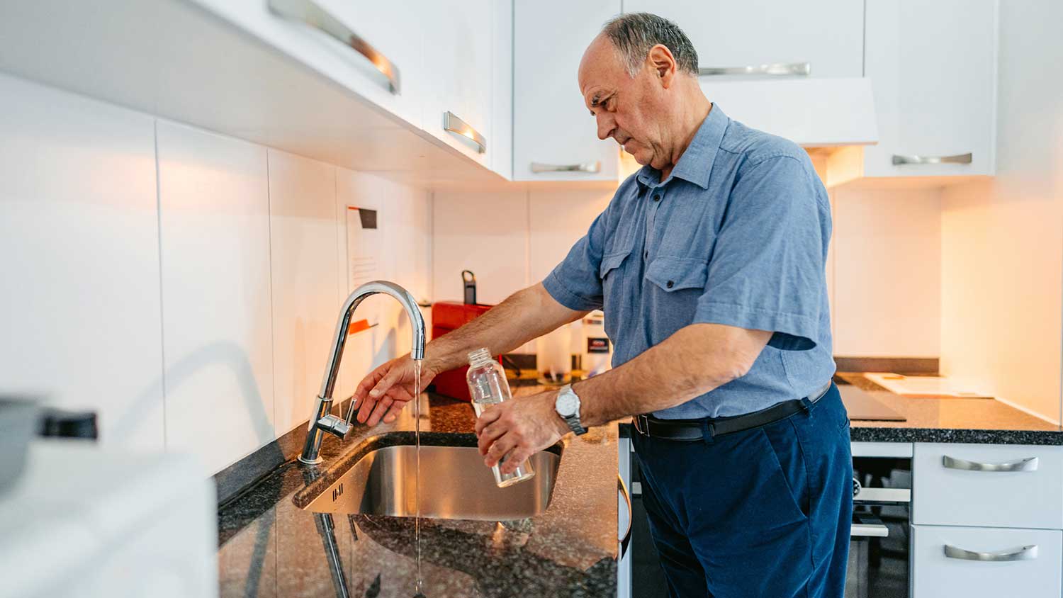 Man in the kitchen filling bottle with tap water