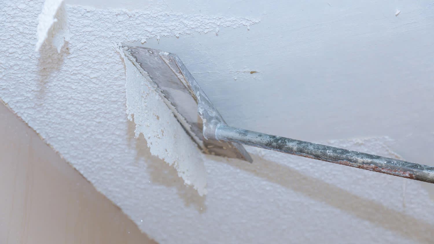 A person scraping off popcorn ceiling