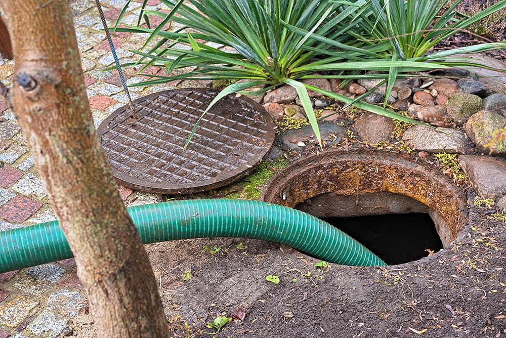 Septic tank with an open cover and green hose for pumping