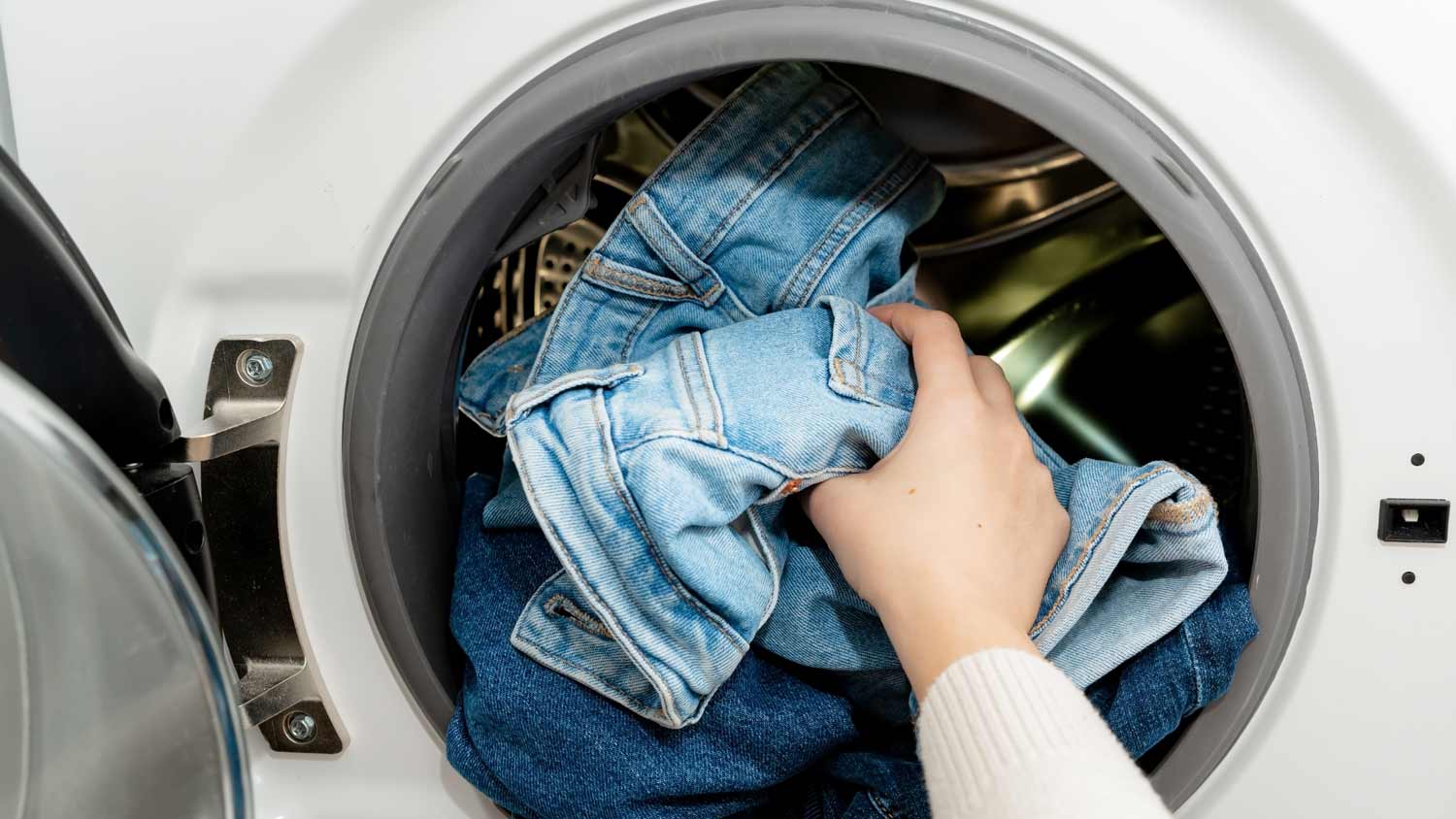 person putting jeans in dryer machine