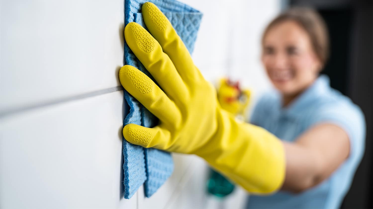 Woman cleaning tile with blue cloth and yellow gloves
