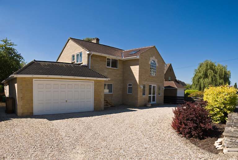 gravel driveway leading up to house and garage with stone siding and blue sky in background