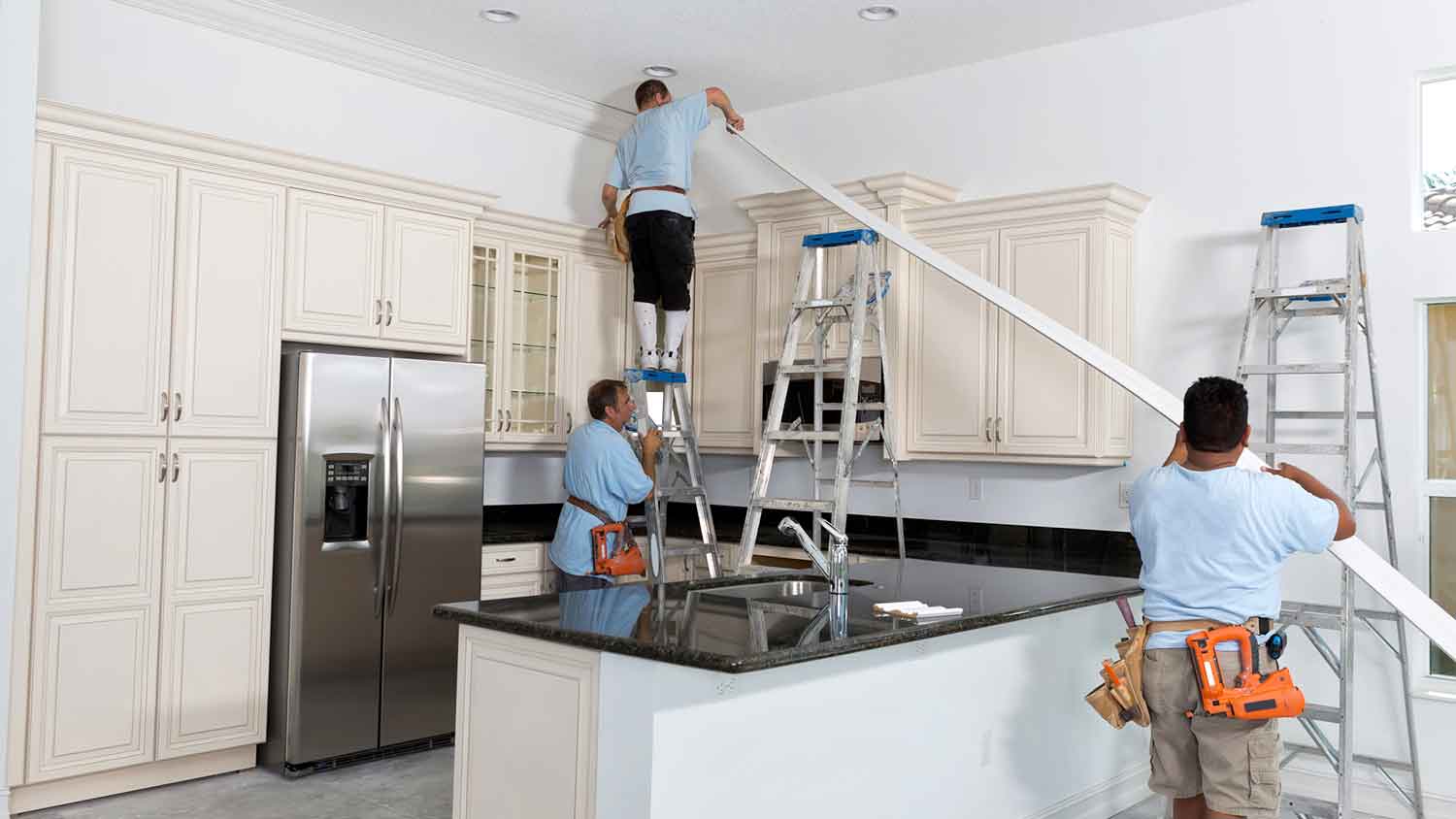 Carpenters installing a long piece of crown molding in the kitchen