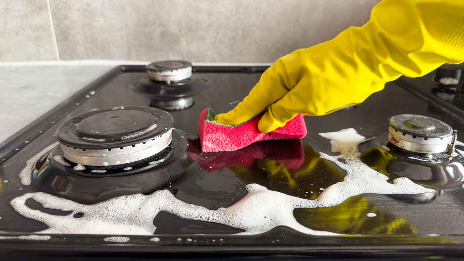Person using soap and sponge to clean a gas stove