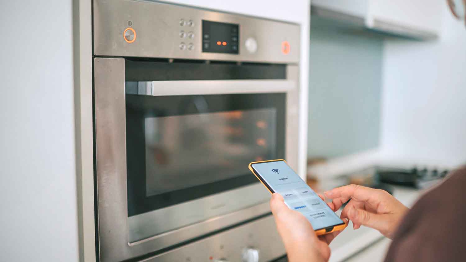 Person using smart phone to adjust kitchen range temperature