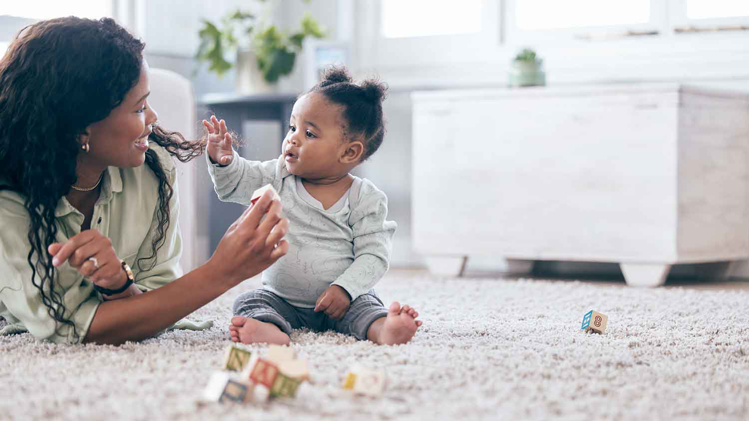 Mother and baby daughter playing on the carpet at home