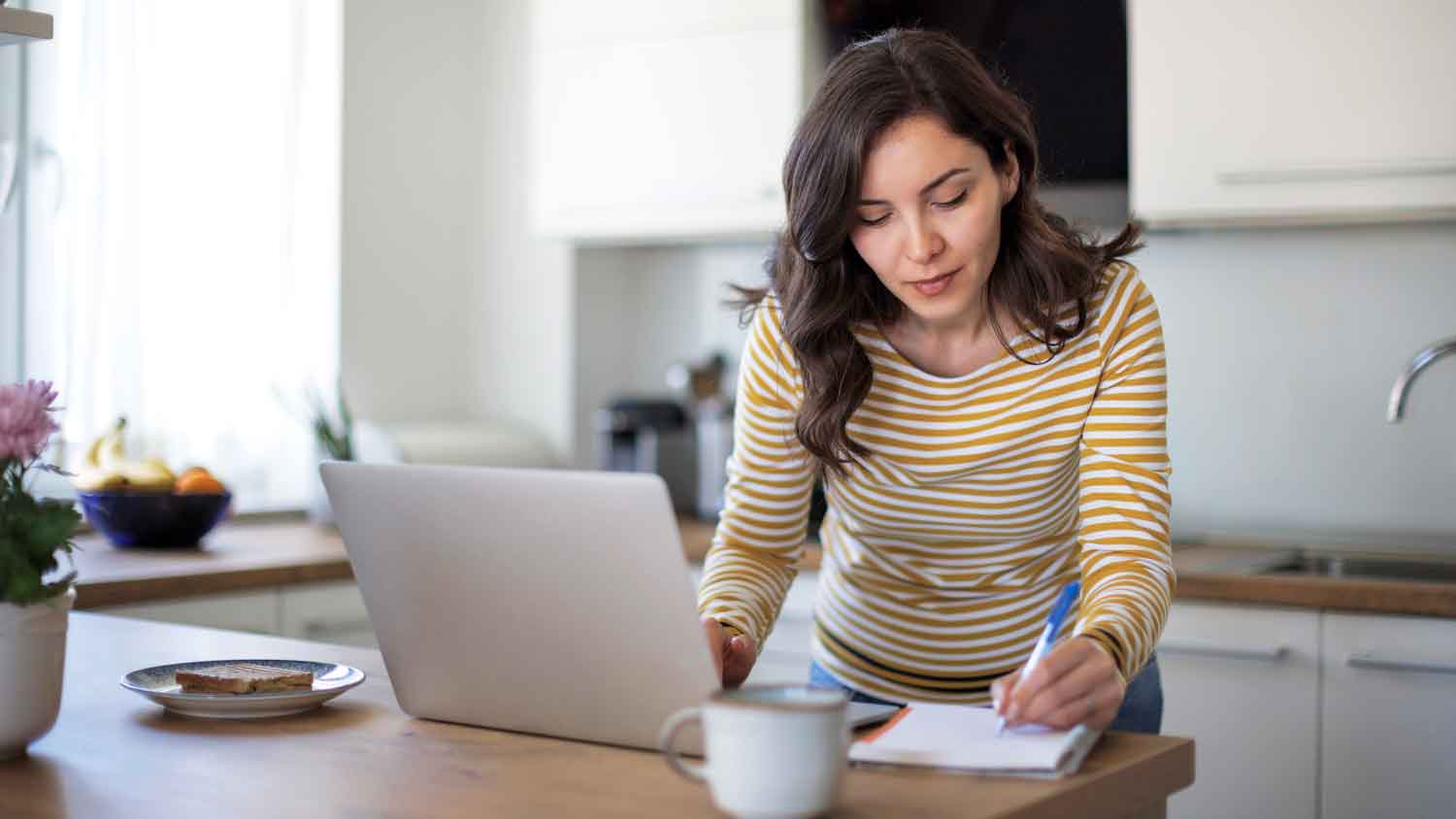 Woman in the kitchen taking notes in a notebook