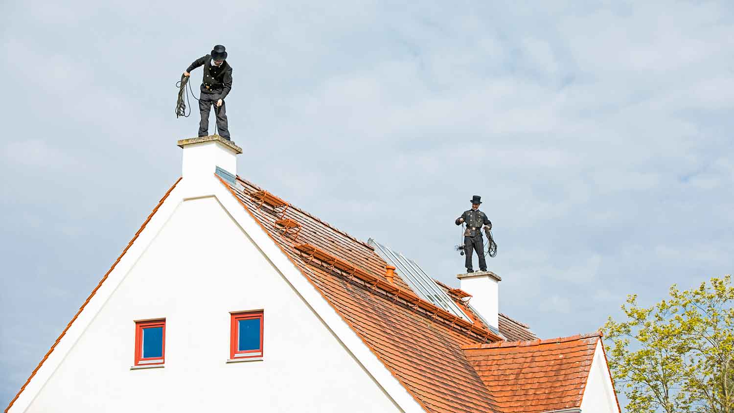 Two chimney sweeps working on the roof of a house