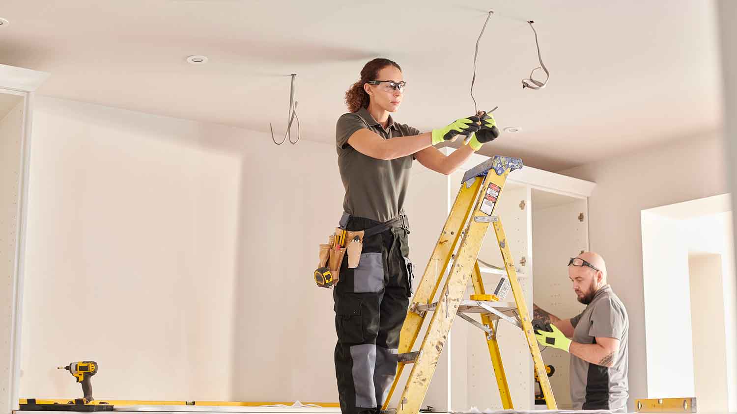 Female electrician on a ladder wiring a new kitchen