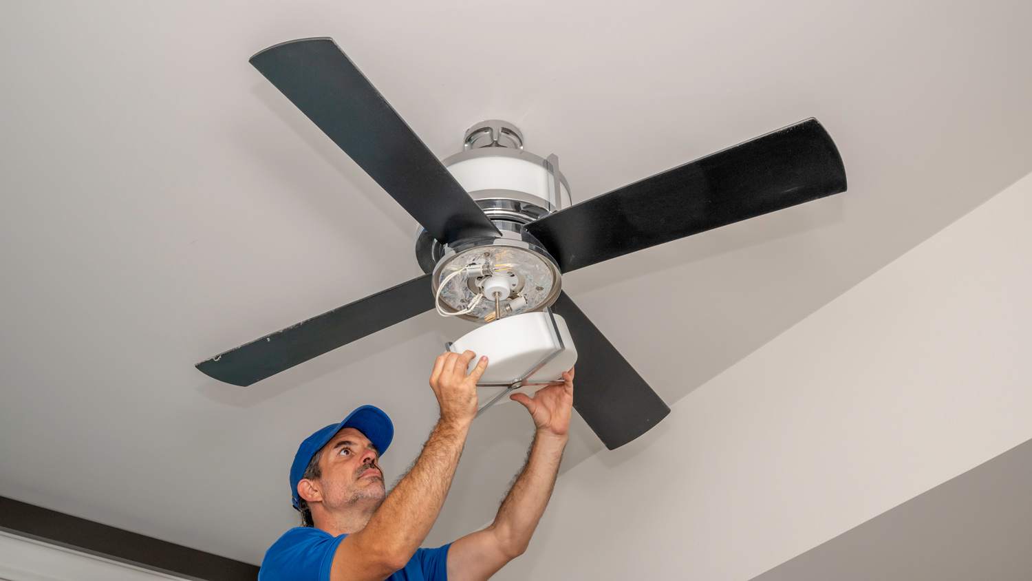 Man removes glass light cover on a ceiling fan inside of a home