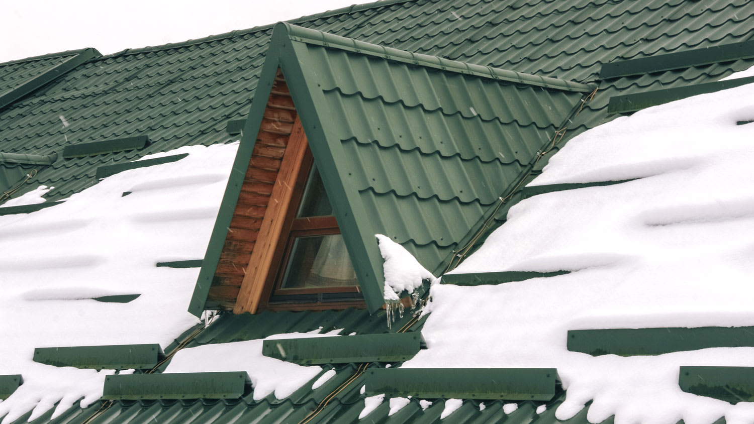 Snow on green metal tiles roof of a european house with window