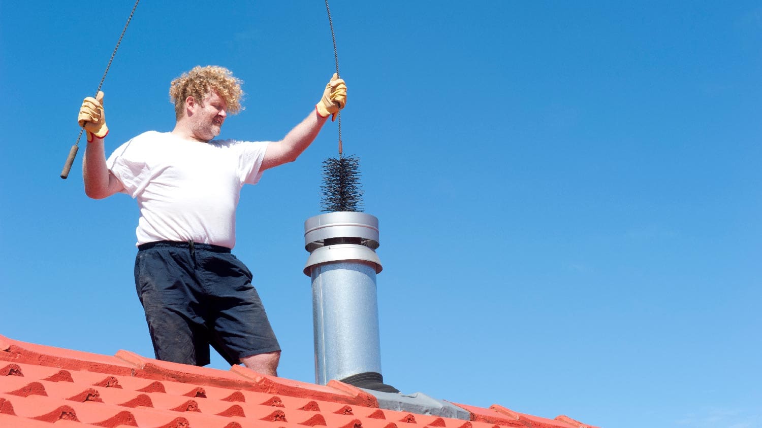A person cleaning a metal chimney on a tiled roof