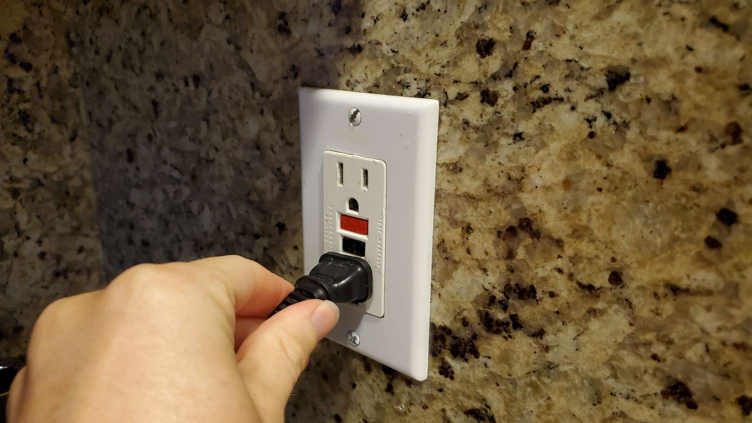 man plugging electrical cord in gfci outlet in kitchen