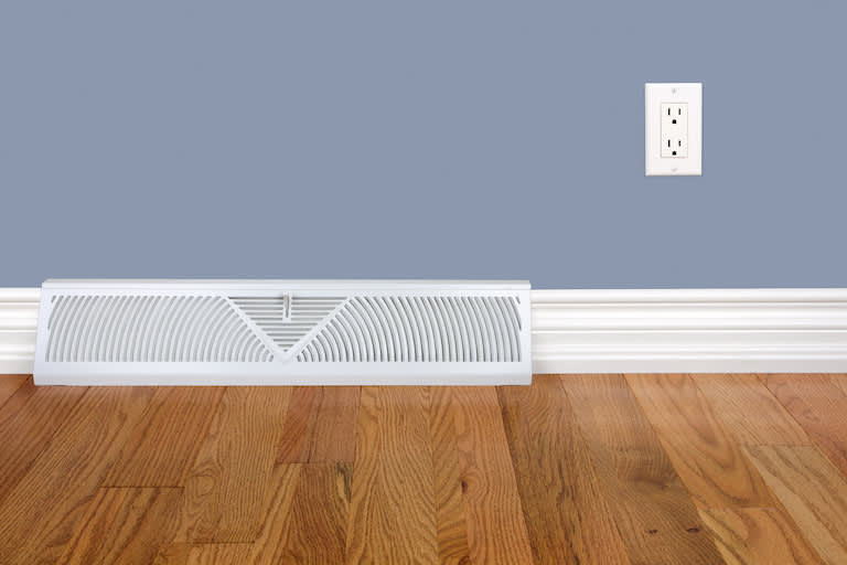 Bedroom wall with heating register, baseboard, electrical outlet and hardwood floor
