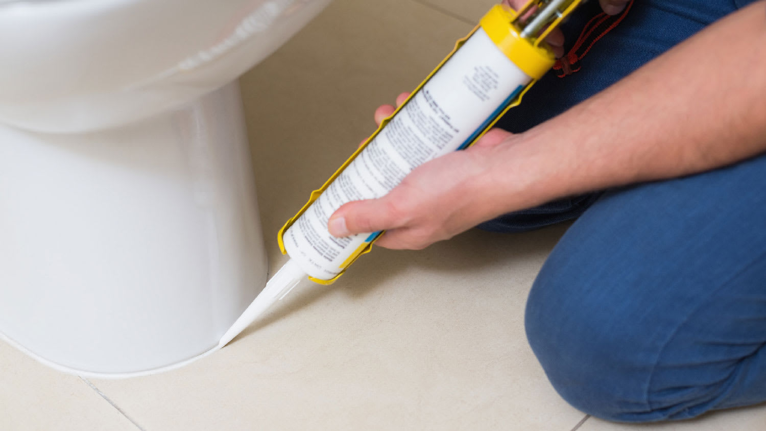 A person re-caulking the toilet