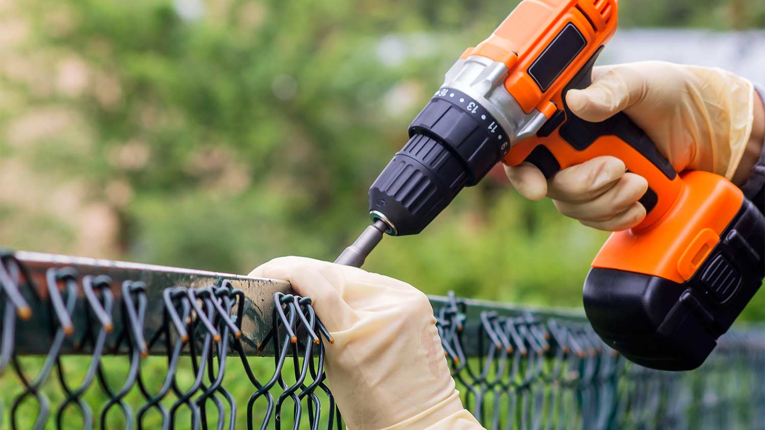 man fastening the metal mesh of a fence with drill