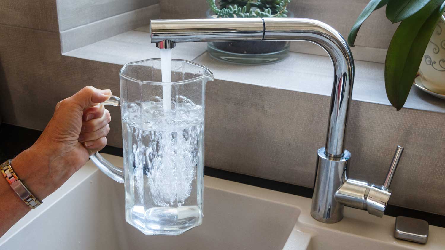 person filling glass jug with water from the faucet