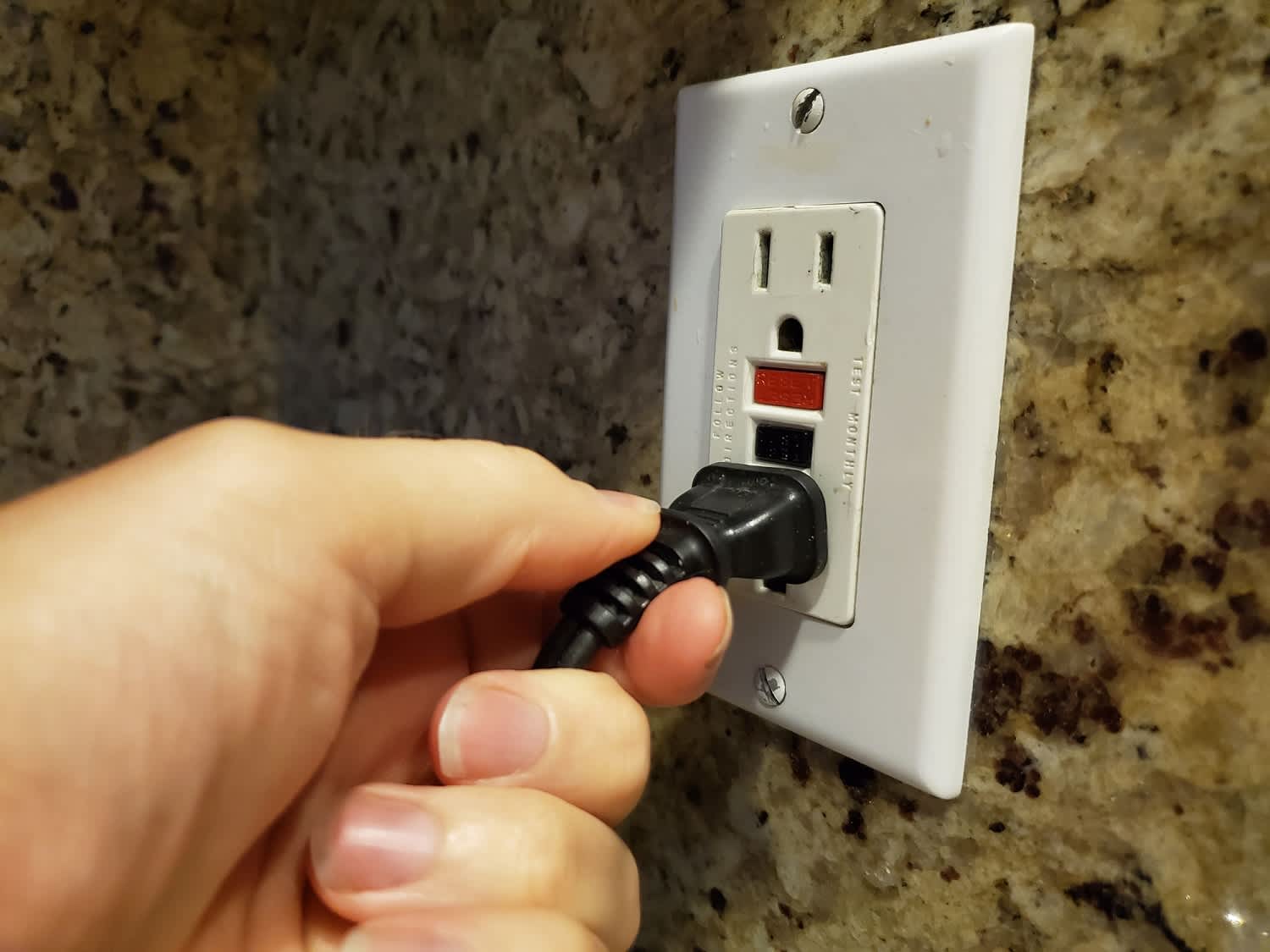human hand of a man plugging an electrical cord into a GFCI electrical outlet