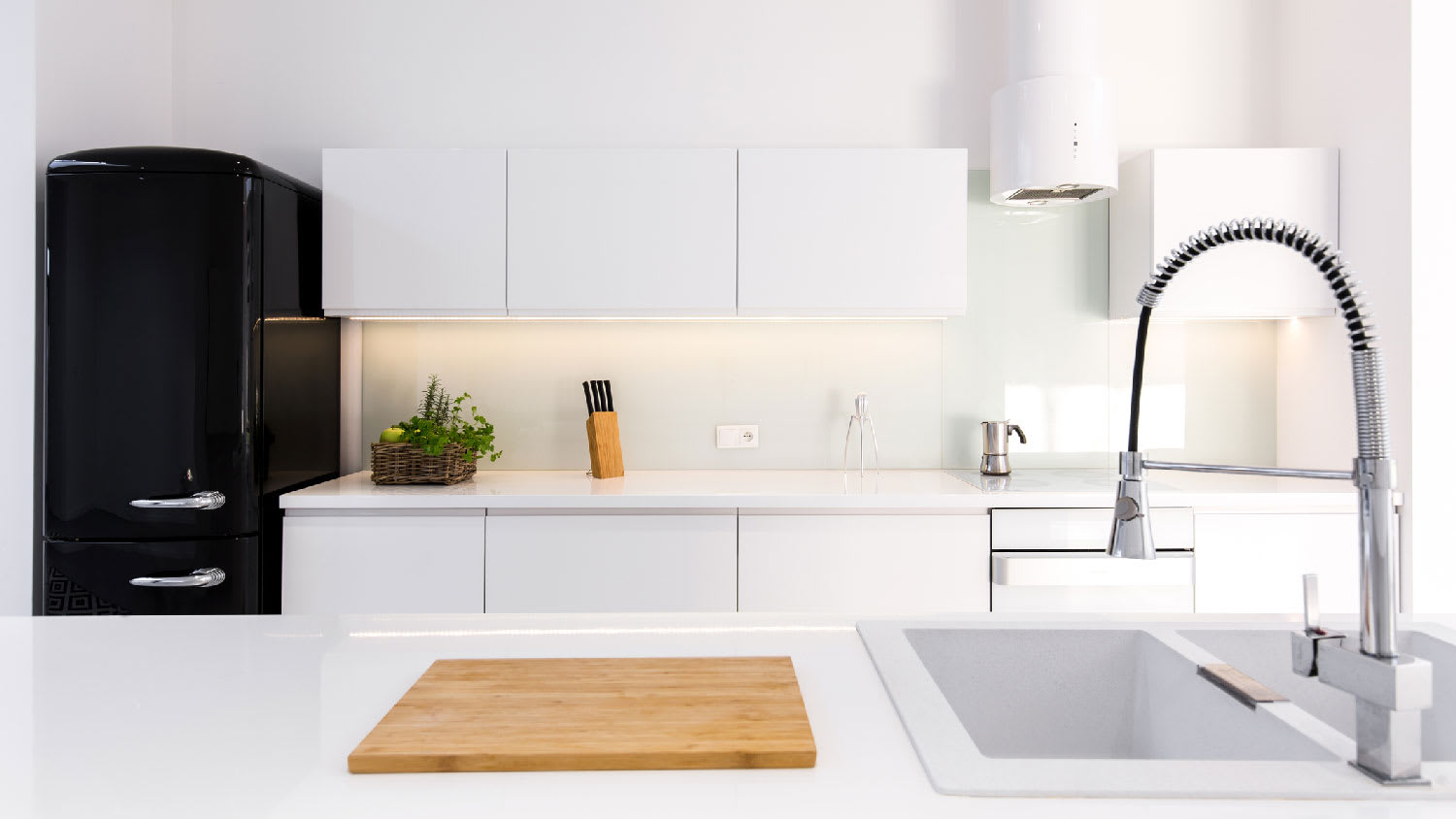 A kitchen with white lacquered cabinets and a black fridge