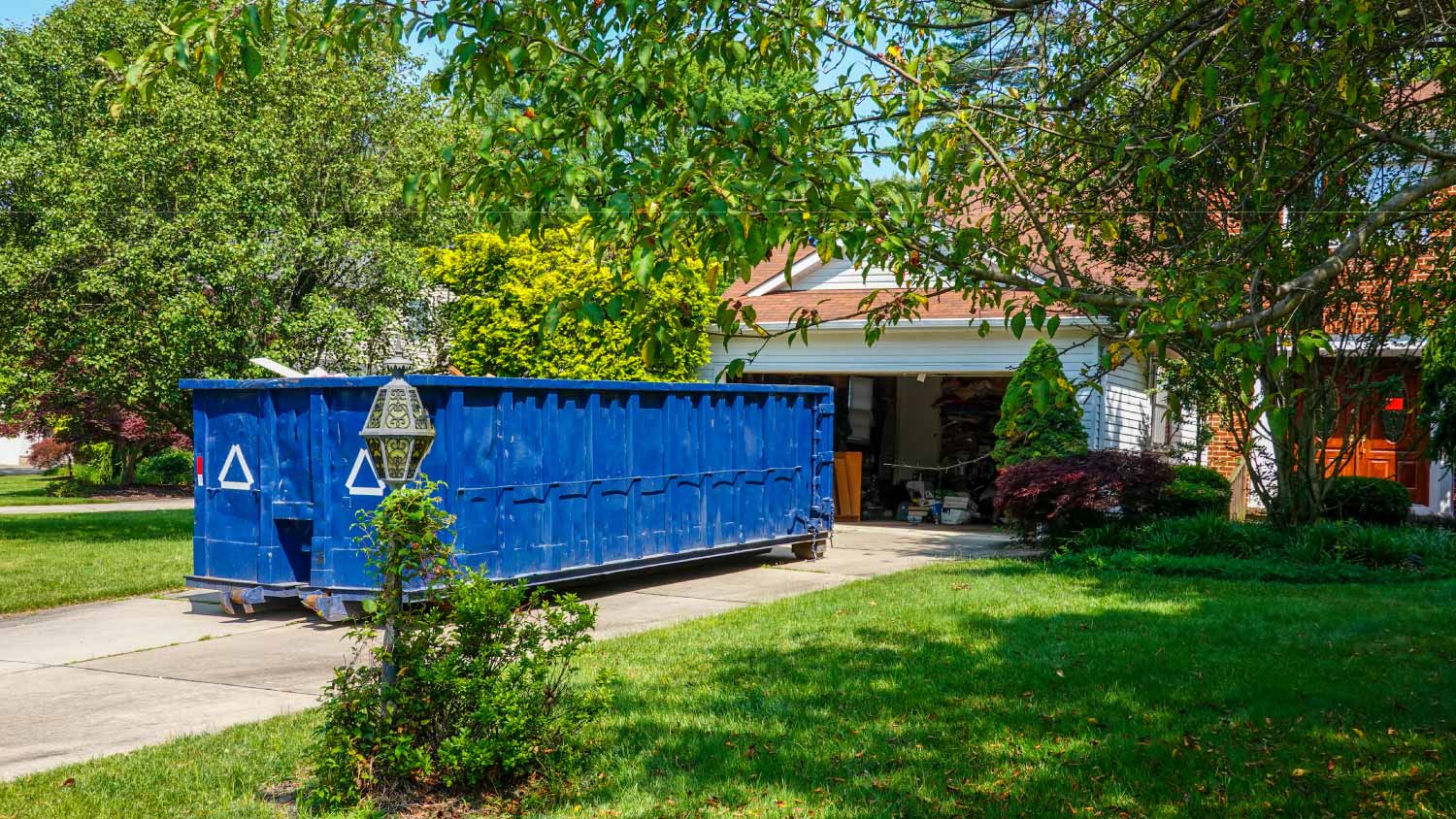An empty blue dumpster in the driveway