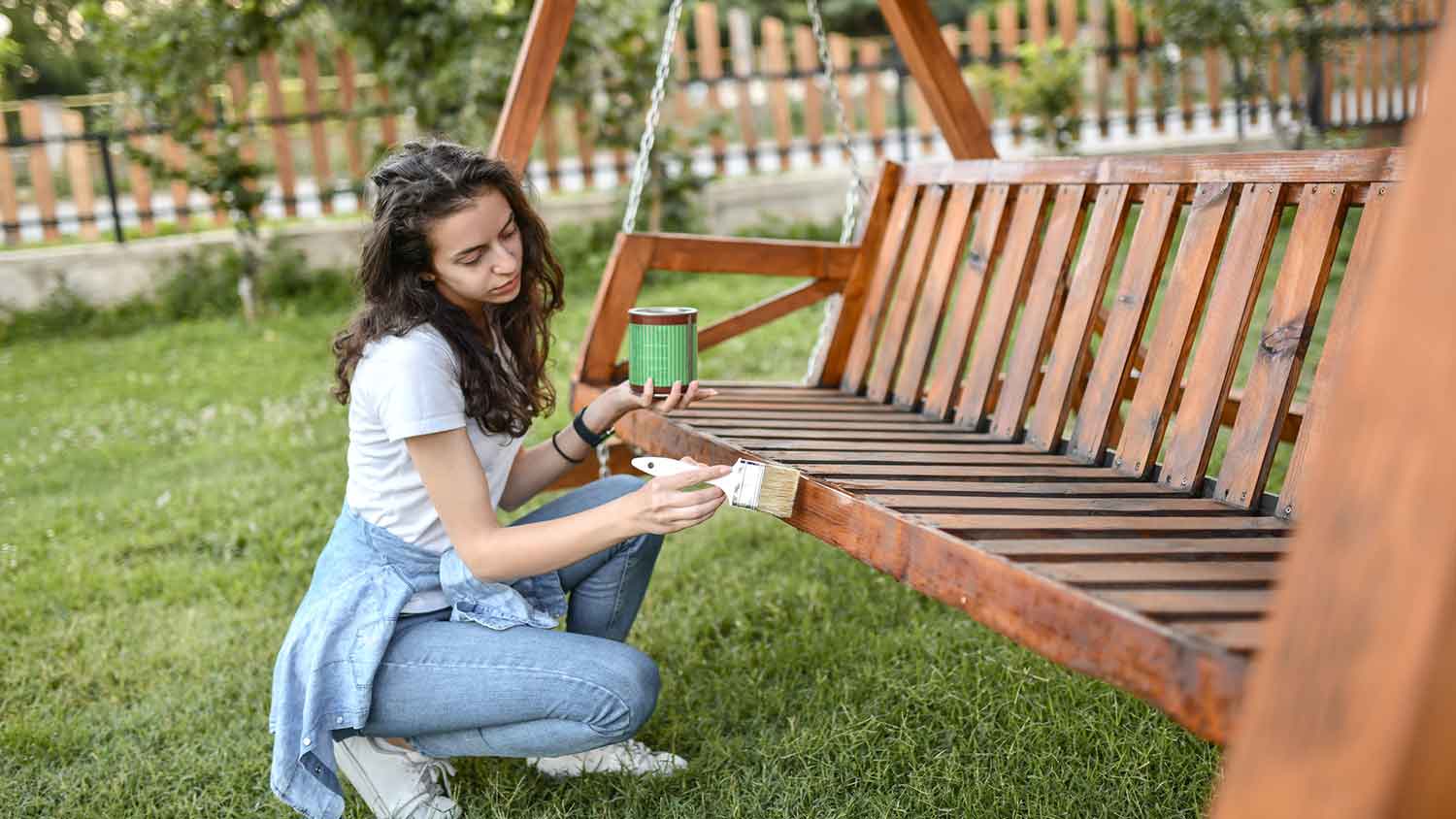 Woman using stain to paint outdoor wooden swing