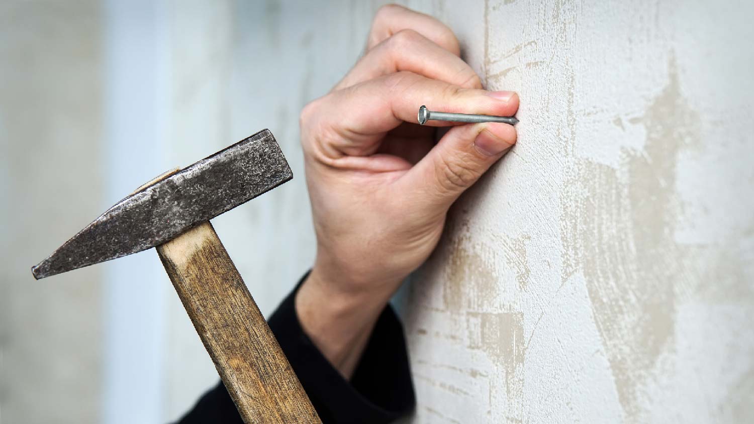 A person holding a nail and a hammer on a drywall