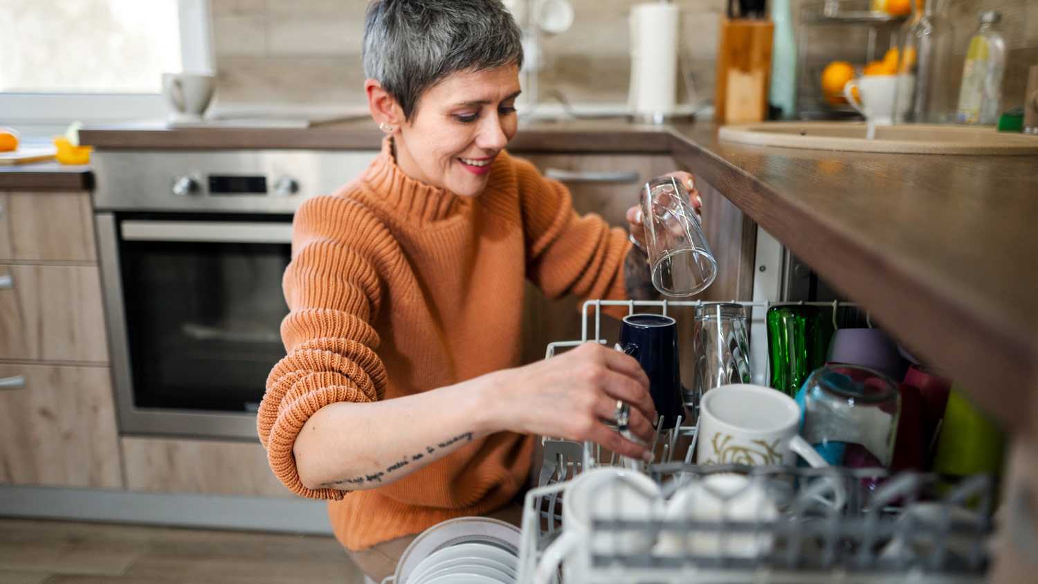 Mature woman with tattoos putting dishes in dishwashe