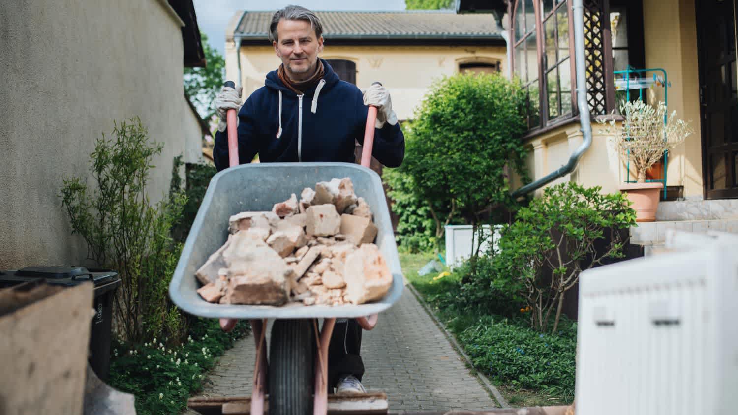 Mature man disposing old plaster with a wheelbarrow outdoor