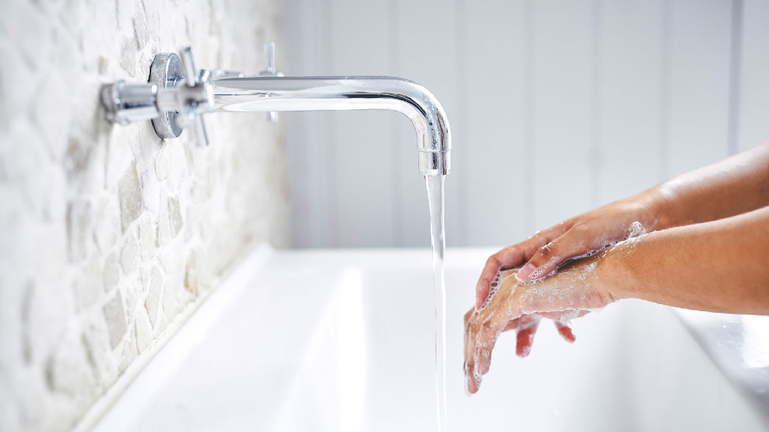 A woman washing her hands on a wall-mounted faucet