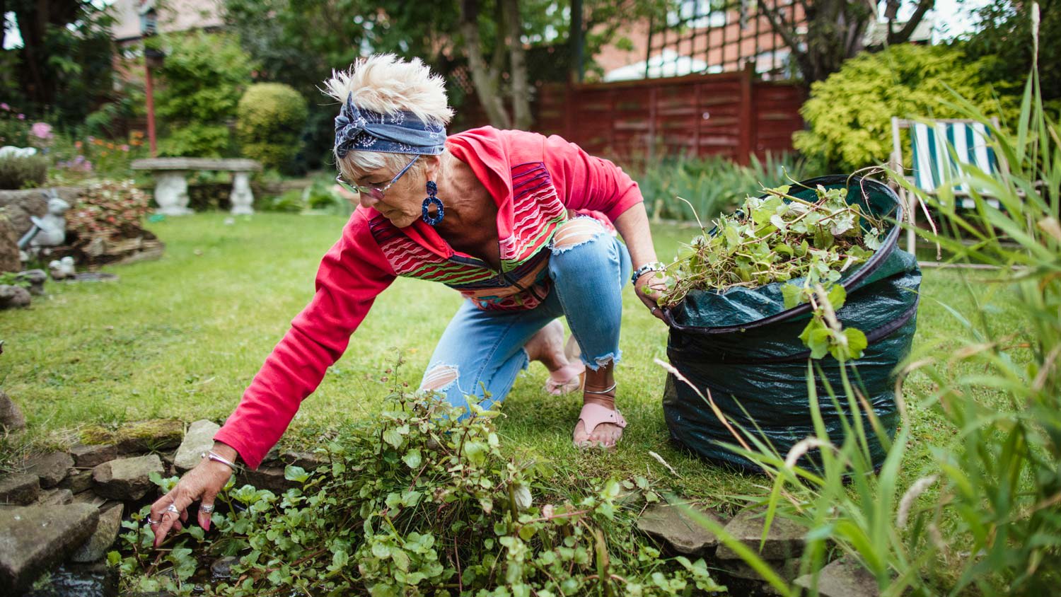 Senior woman gathering weeds and garden waste in her compost bag