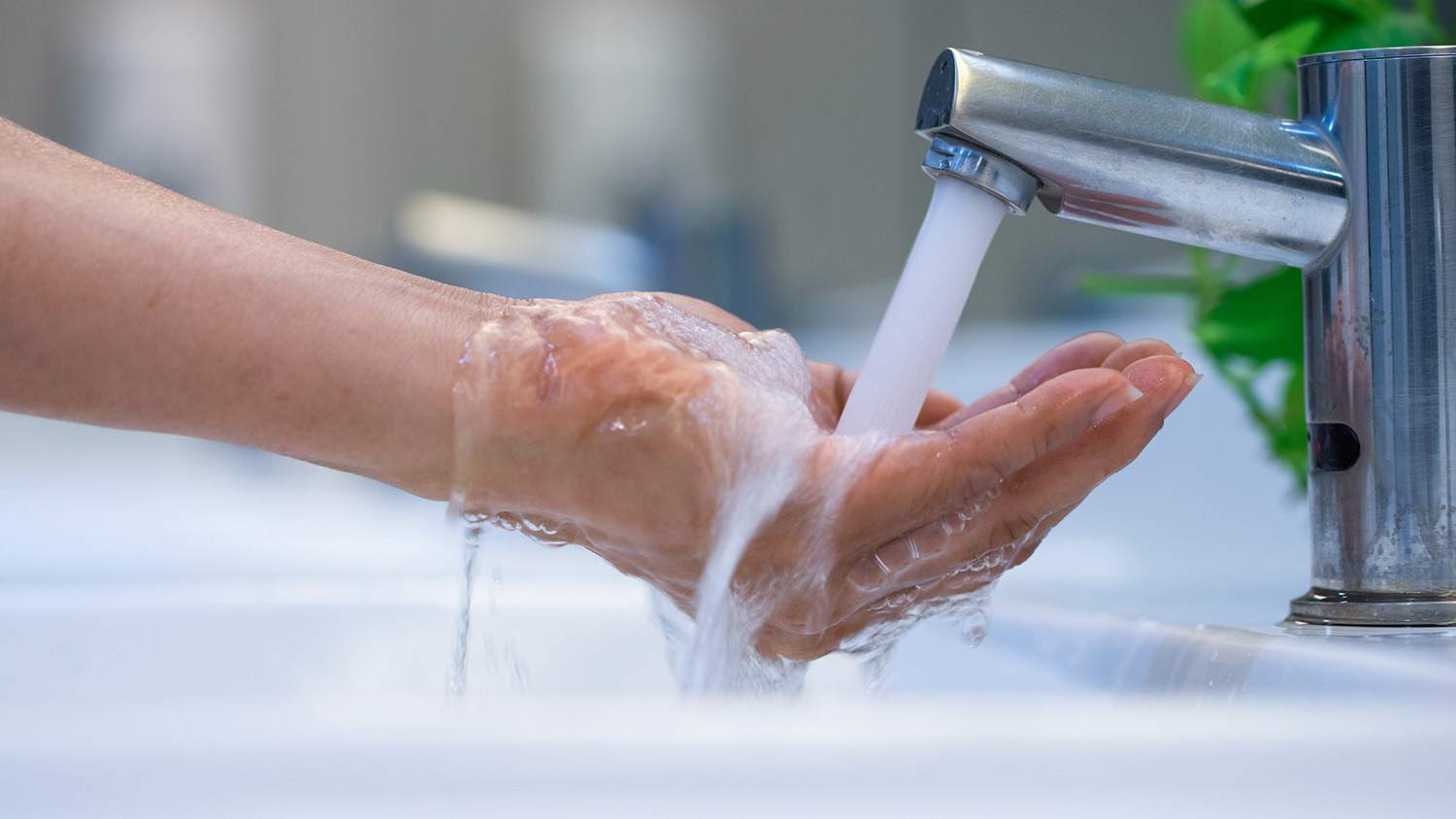 Woman washes hand under touchless faucet
