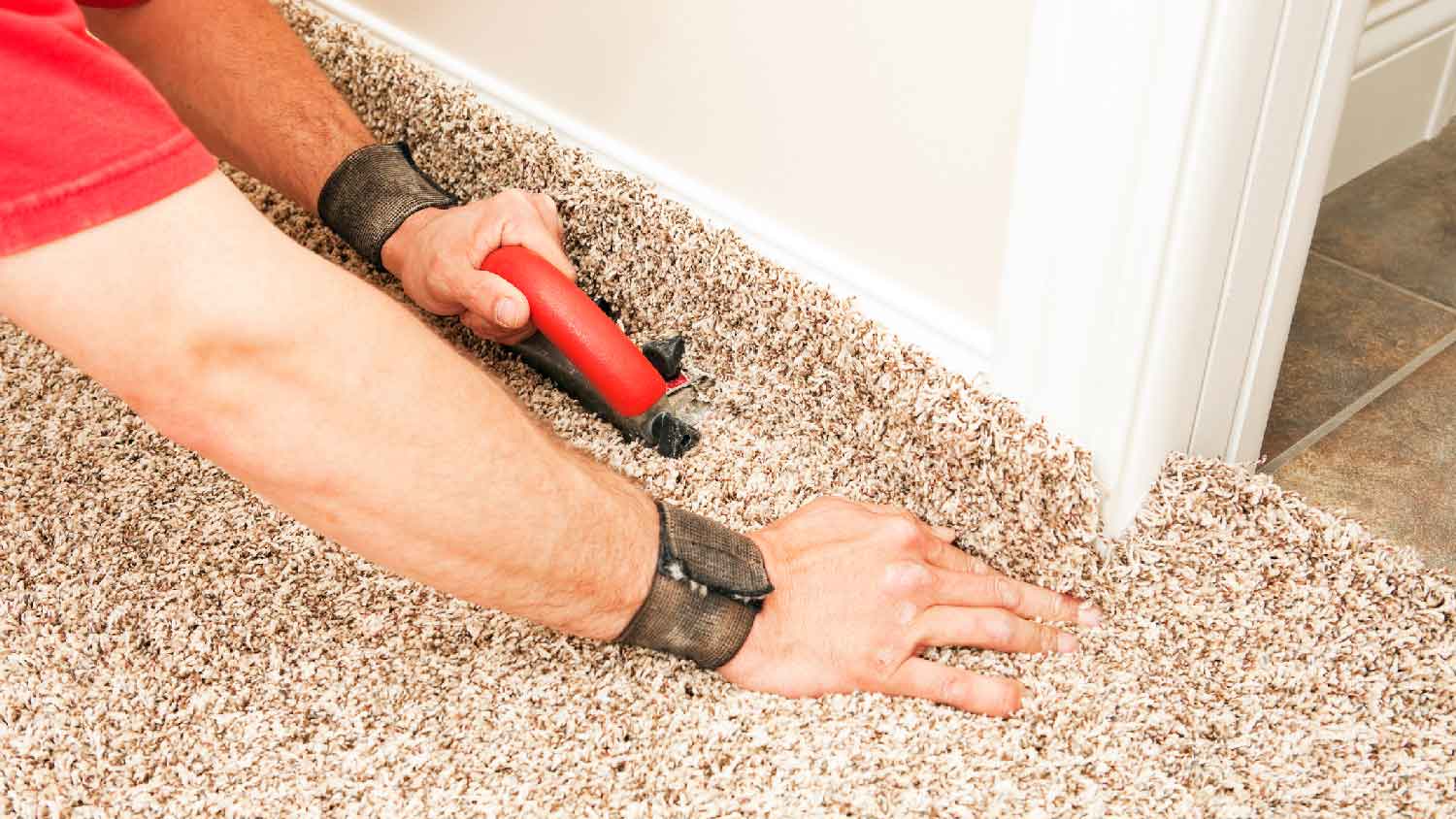 A man installing a carpet’s edge next to a baseboard