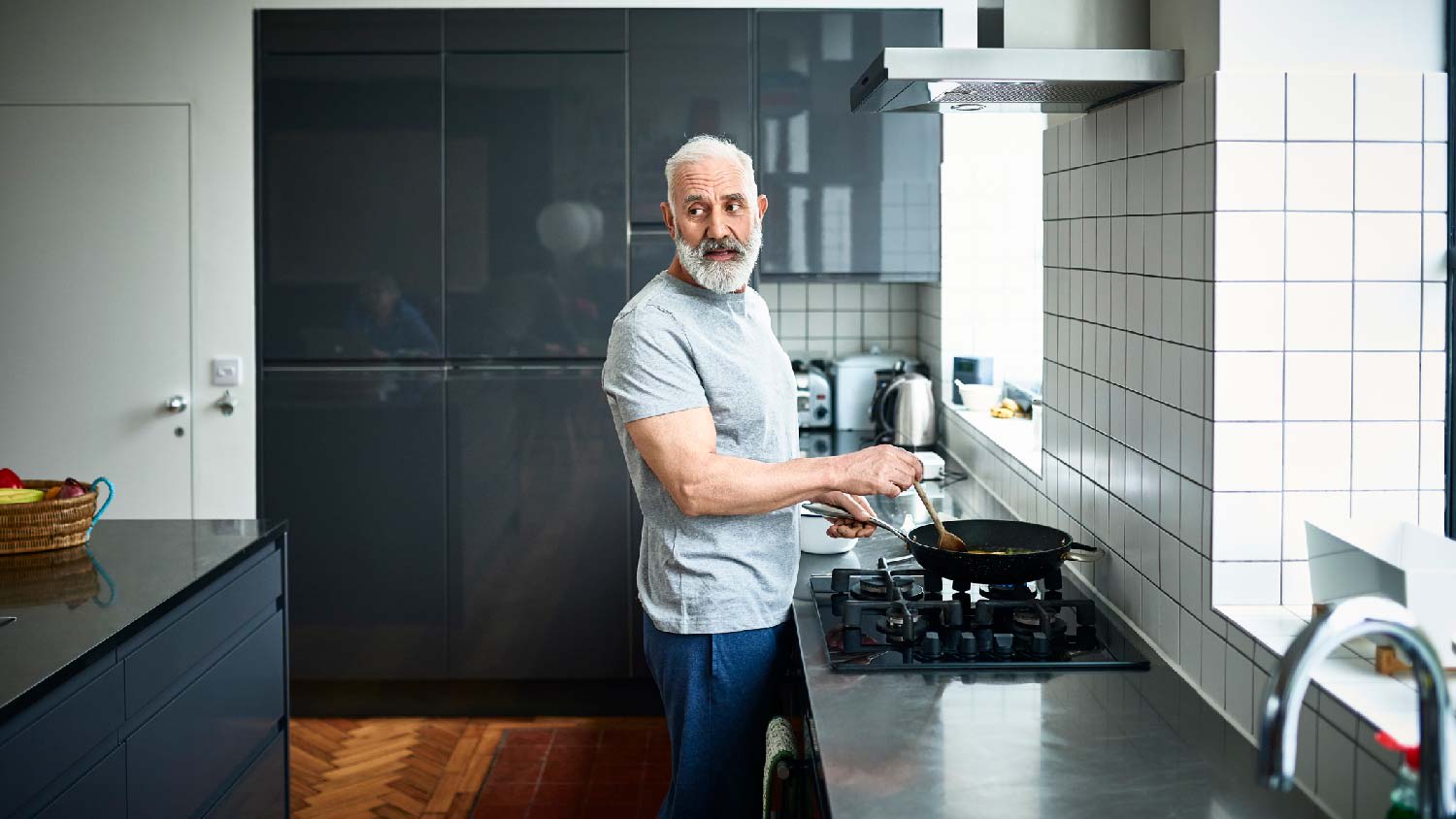 A senior man cooking on his stove in front of a tiled backsplash