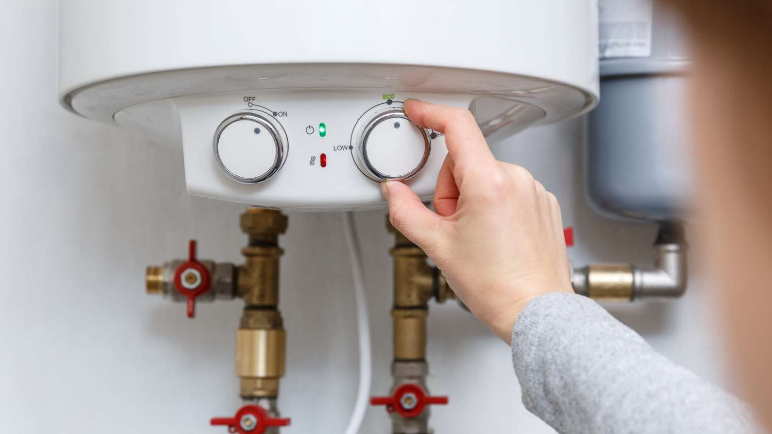 Female hand puts thermostat of electric water heater
