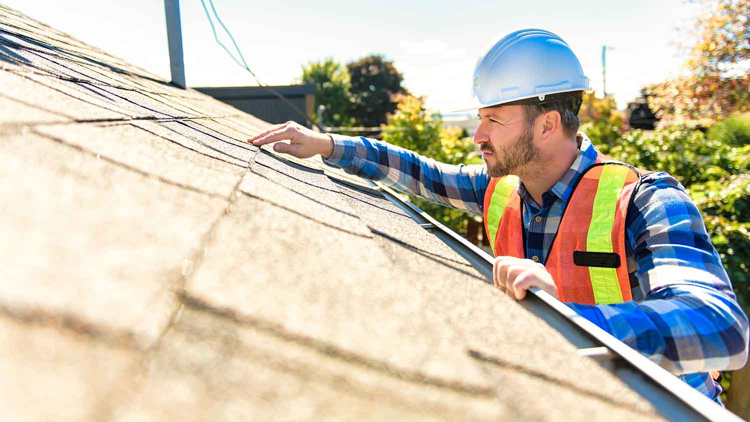 Roofer wearing a helmet is inspecting the roof of the house