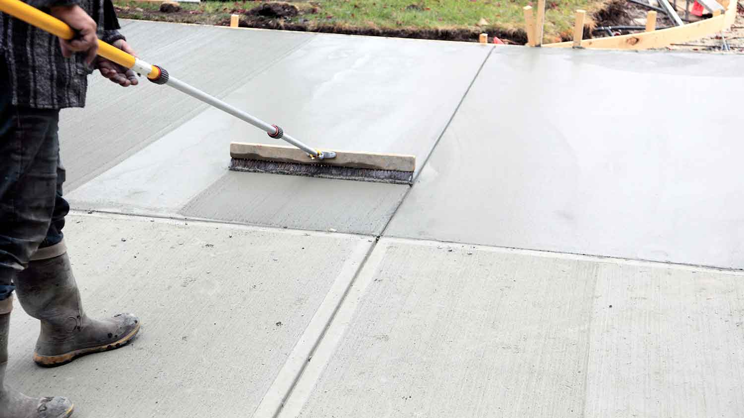 worker using shop broom to create surface on concrete driveway