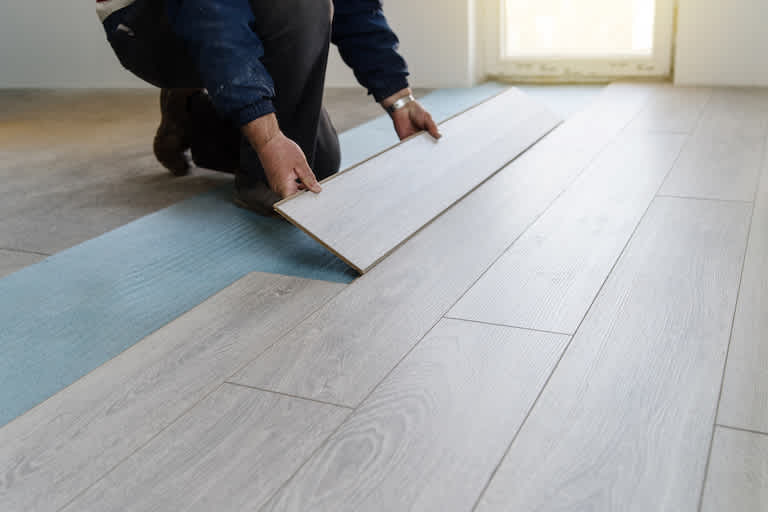 worker installing grayish tan slabs of laminate flooring