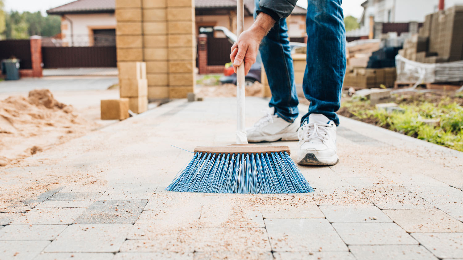A man with a brush sweeps the paving slabs on the path near the house