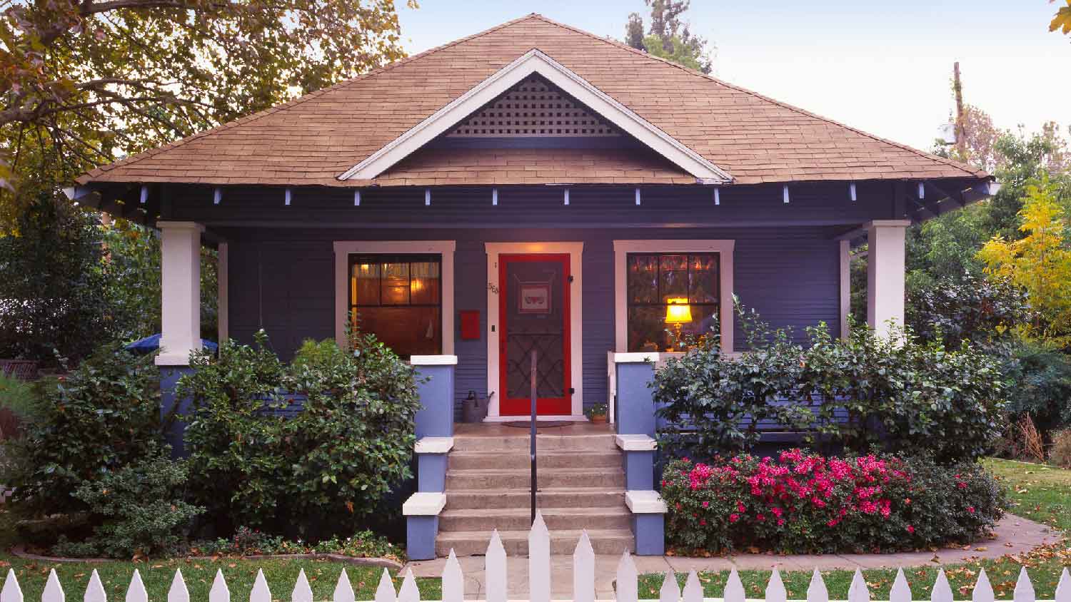 A bungalow with a hip roof and a white picket fence