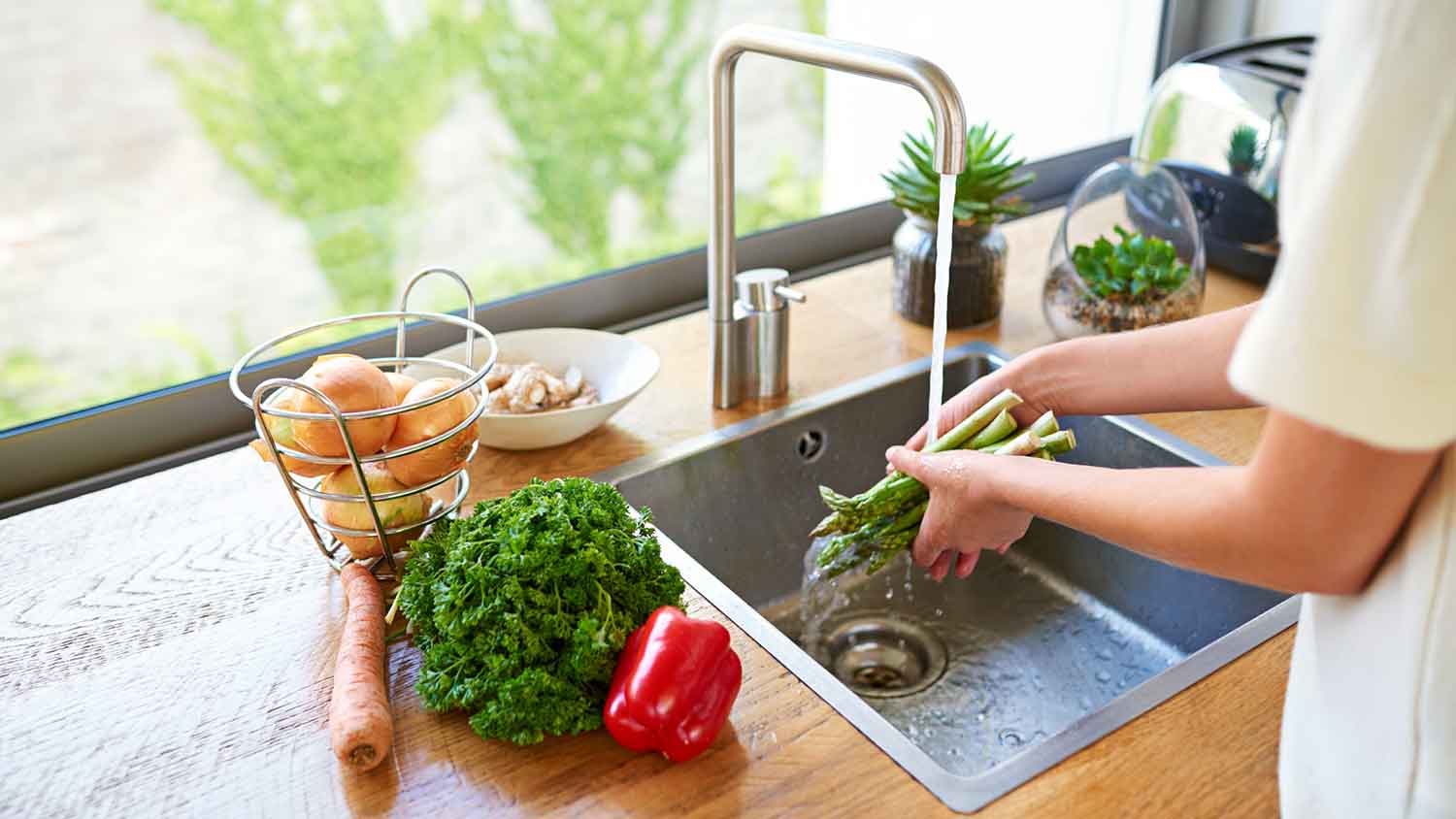 Woman washing veggies in a stainless-steel kitchen sink