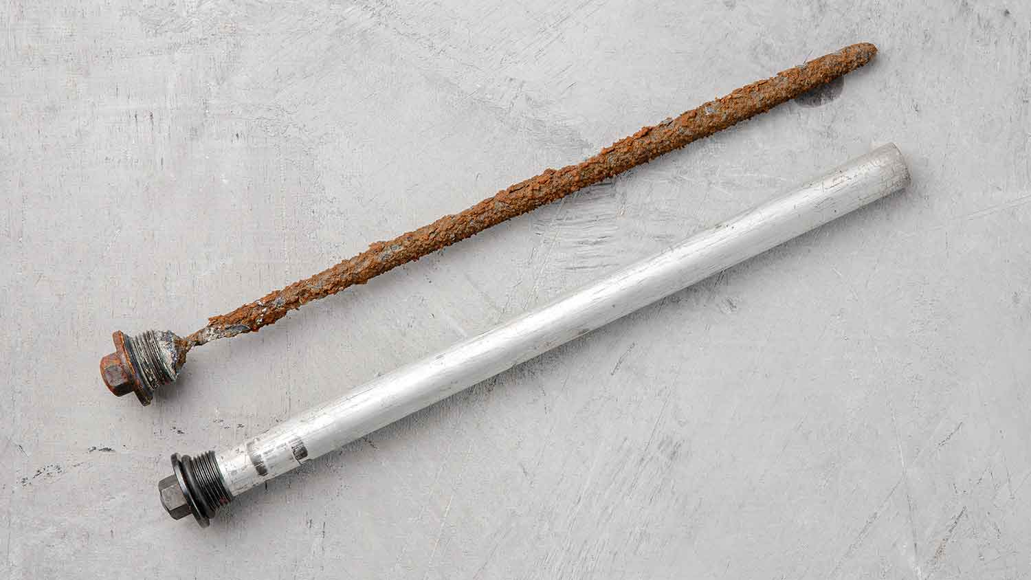 Old and new sacrificial anode rods on a gray surface